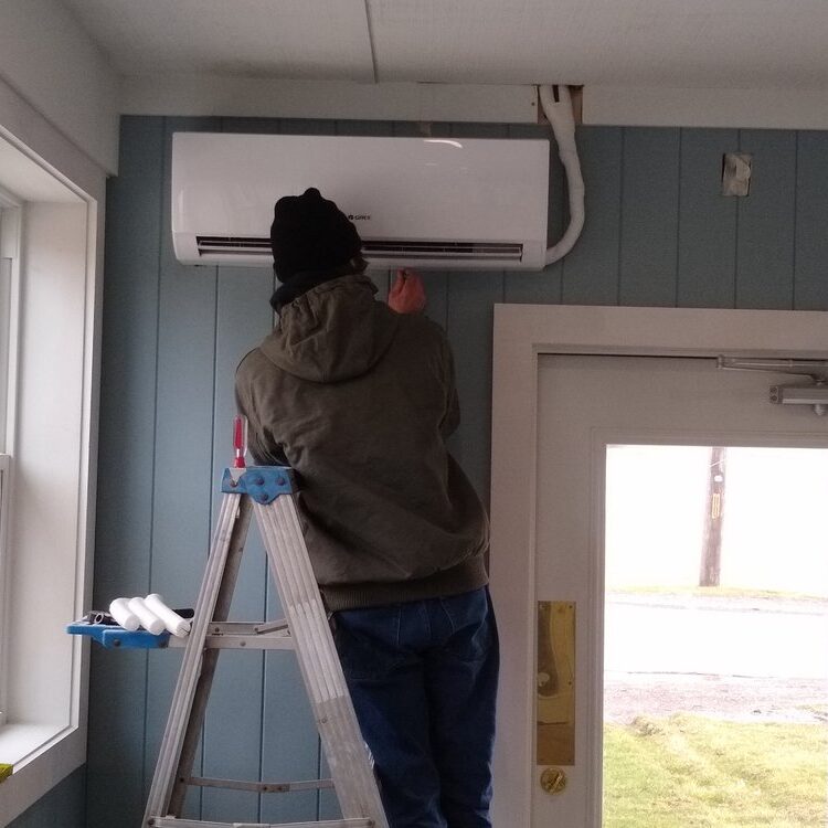 A man on a ladder working on an air conditioner.